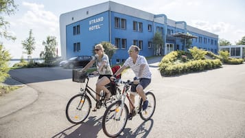 Zwei Personen mit Fahrrädern vor einem blauen Gebäude mit der Aufschrift 'STRAND HOTEL'.