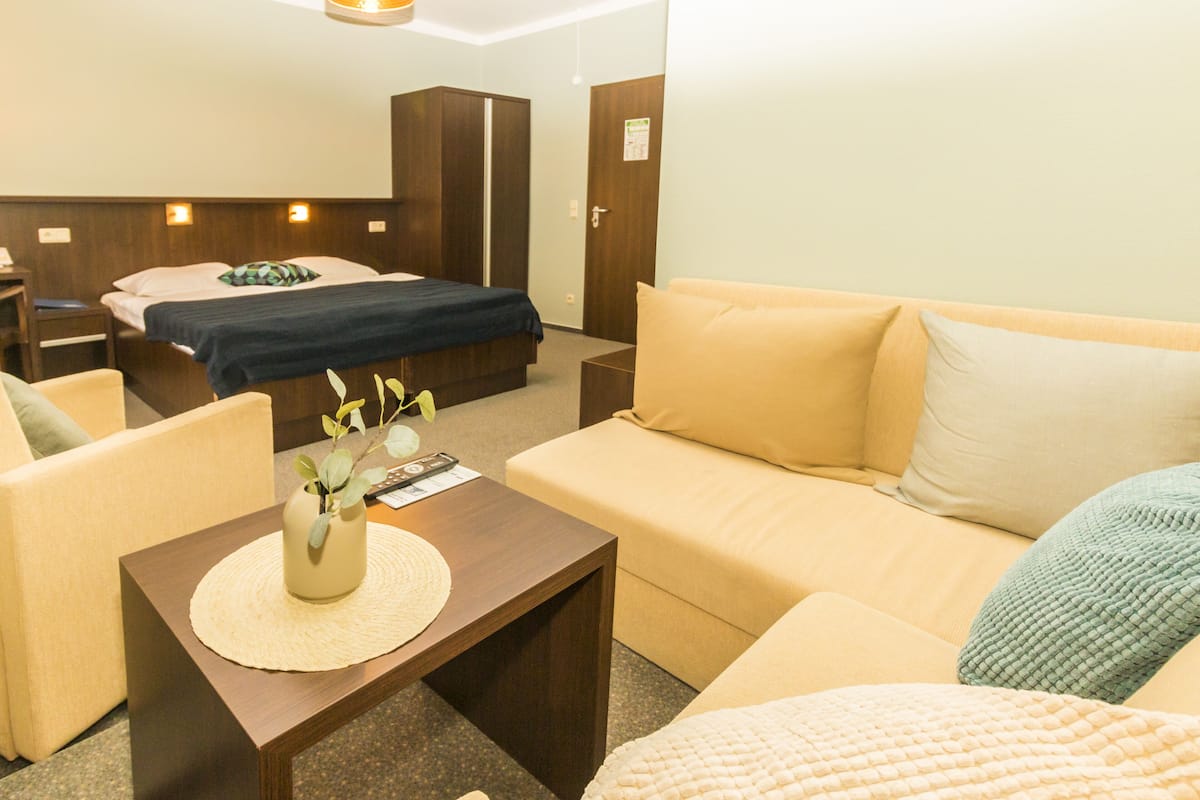 A hotel room with a bed, a sofa, a small table with a vase, and a nightstand.