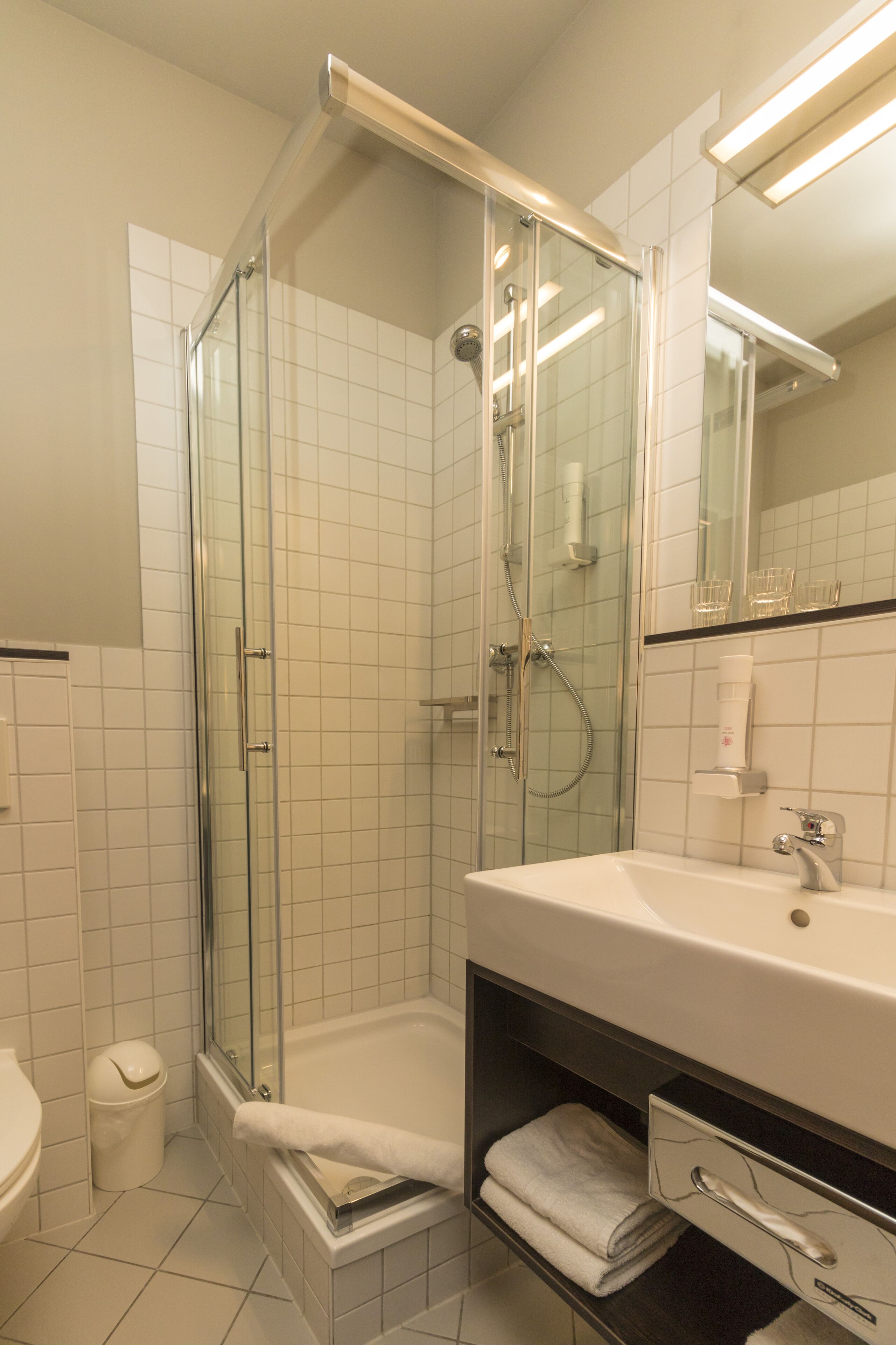 Ein modernes Badezimmer mit einer Duschkabine aus Glas, einem weißen Waschbecken und einem Spiegel darüber.