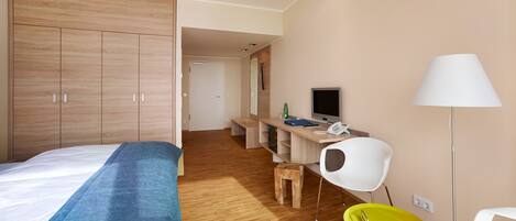 A hotel room with a bed, a desk with a computer, a chair, and a lamp.