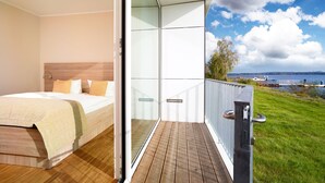 A bedroom with a bed and a balcony with a view of a lake and a boat. - Strandhotel Senftenberger See (Senftenberg)