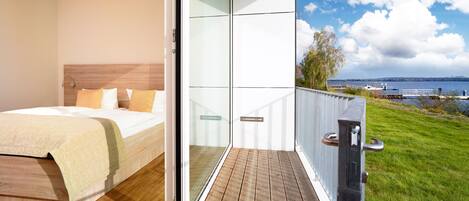A bedroom with a bed and a balcony with a view of a lake and a boat.