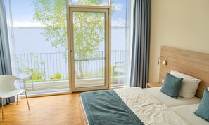 A bedroom with a large window, a bed with pillows, a chair, and a wooden headboard. - Strandhotel Senftenberger See (Senftenberg)