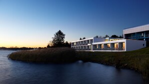 A modern building with a flat roof and large windows, situated by a calm body of water. - Strandhotel Senftenberger See (Senftenberg)
