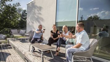 A group of people sitting on outdoor furniture on a wooden deck, with a modern building in the background.