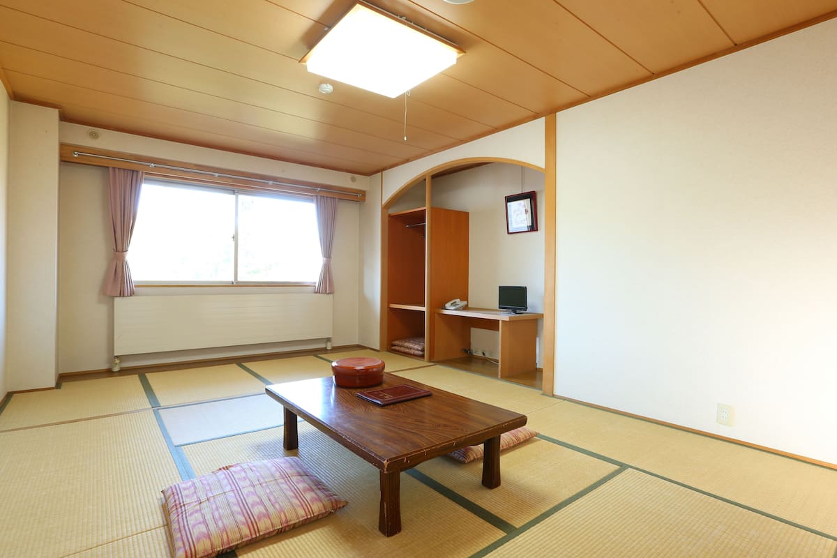 A traditional Japanese room with tatami flooring, a low wooden table, a futon, and a sliding door closet.