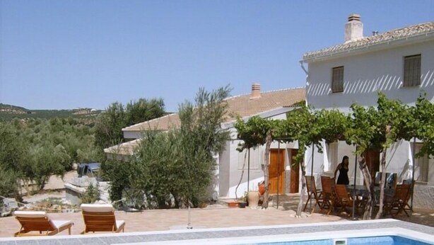 A swimming pool with wooden loungers, a covered seating area, and a white building with a tiled roof. - Lasnavillasmm (Montefrio)