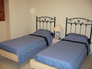 A twin room with two single beds, each with a blue bedspread and black headboard. There is a bedside table with a lamp and a clock. - Lasnavillasmm (Montefrio)