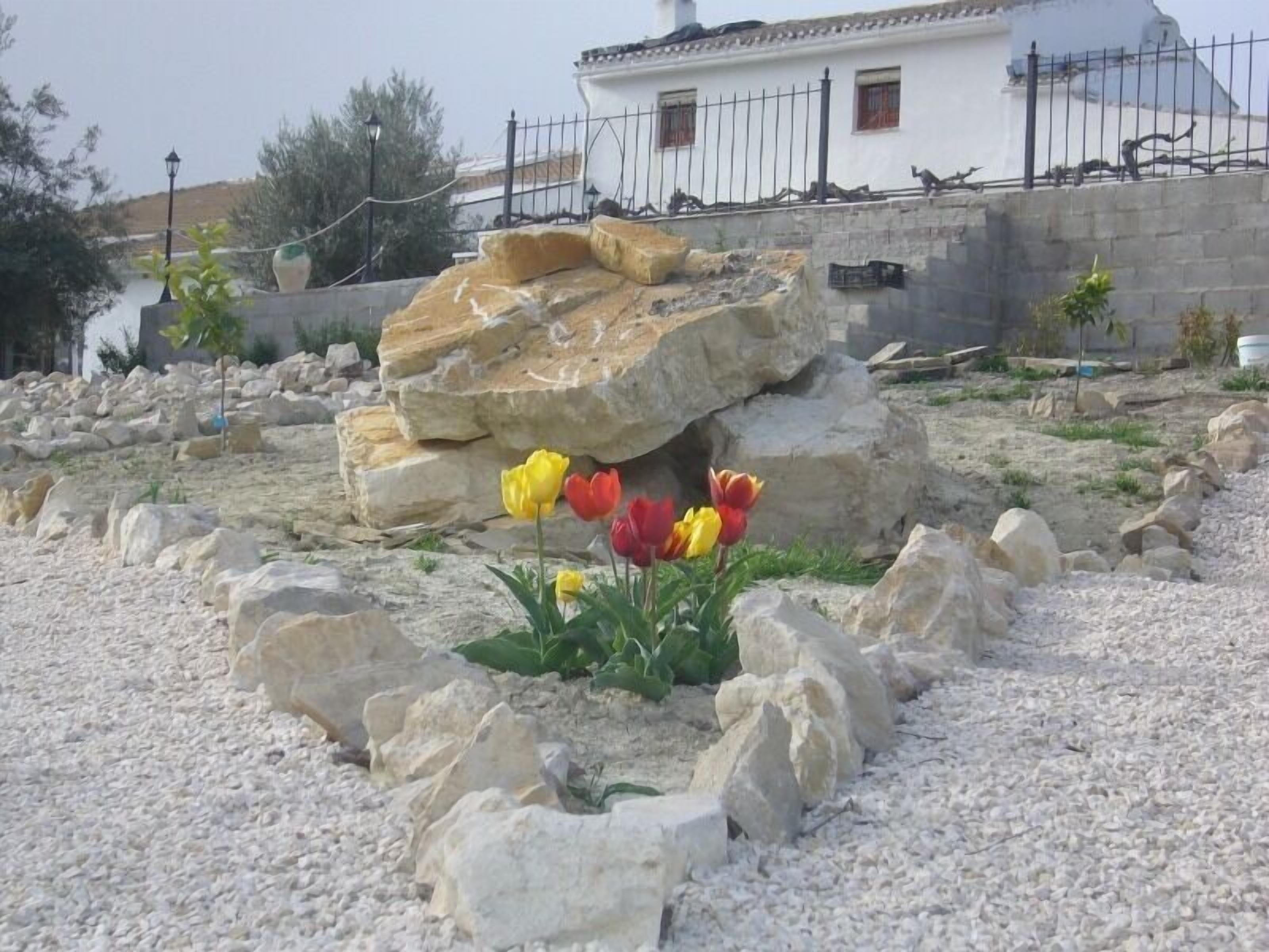 A garden with large rocks, a white building, and a few yellow and red tulips.