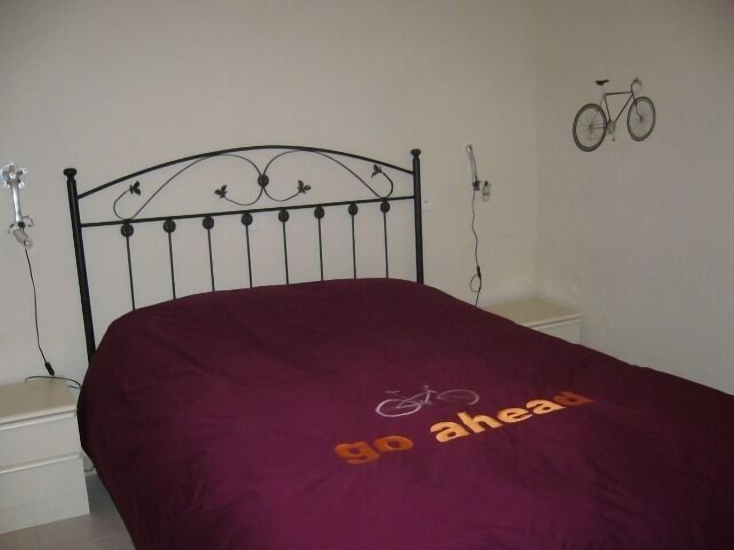 A bed with a purple bedspread that has the text "go ahead" and a bicycle drawing.