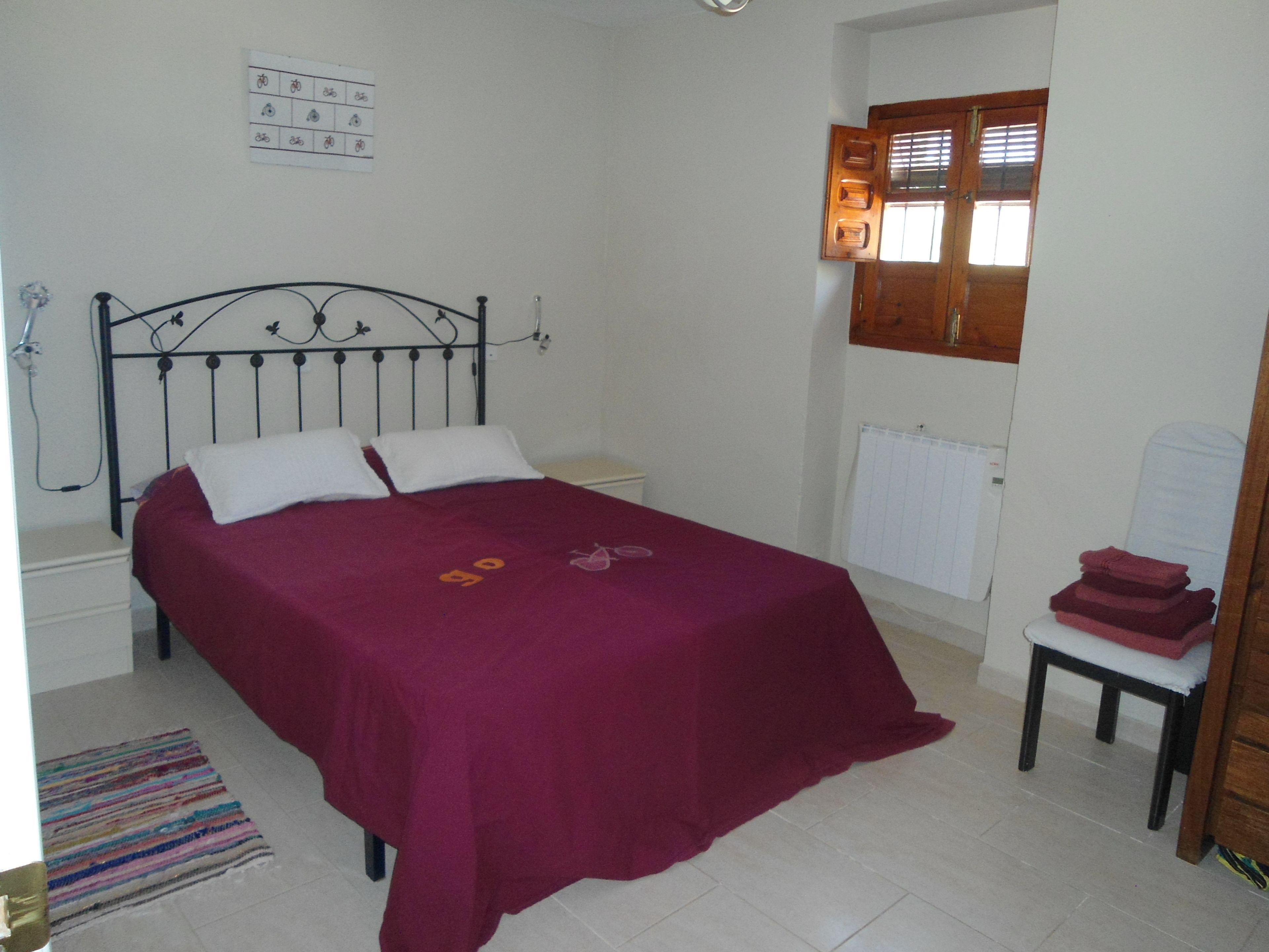 A bedroom with a bed, a nightstand, a radiator, and a window with blinds.