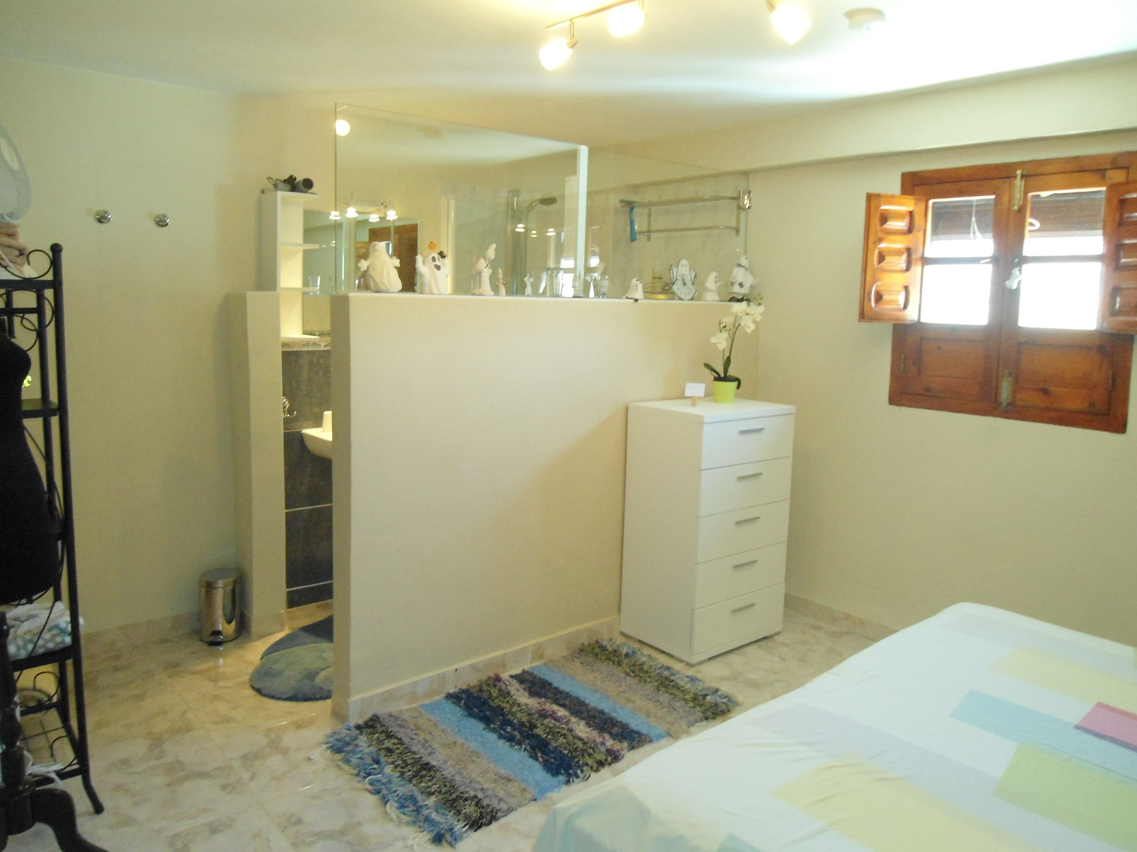A bedroom with a bed, a dresser, a mirror, a window, and a small bathroom with a toilet and sink.