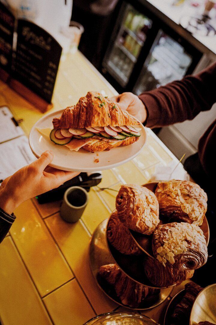 A person holding a plate with a croissant sandwich and a bowl of pastries.