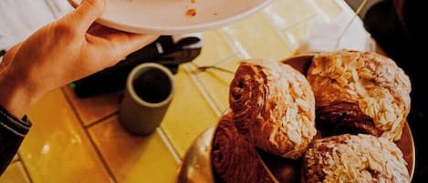 A person holding a plate with a croissant sandwich and a bowl of pastries.