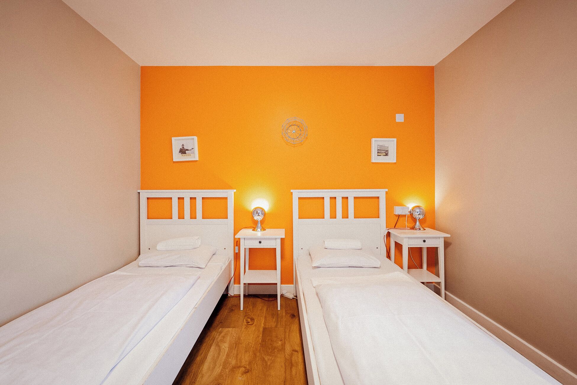 A room with two beds, each with a white headboard and a bedside table with a lamp.