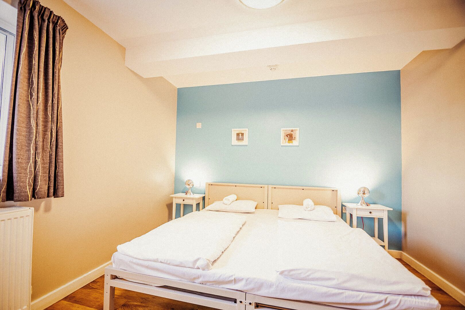 Un letto matrimoniale con lenzuola bianche, due comodini con lampade, una parete blu e un termosifone.