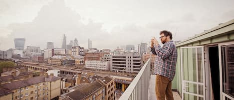 A person standing on a balcony with a cityscape view, including buildings and a bridge.