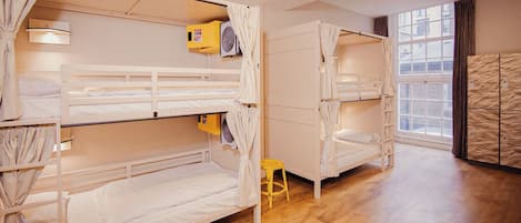 A room with bunk beds, a small stool, and a window with curtains.