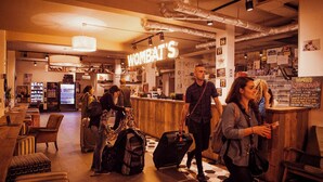 Un espace bar avec un panneau néon indiquant « WOMBAT'S » et un comptoir où est affiché le menu. On y trouve des chaises et des tables, et un réfrigérateur est visible au fond.