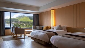 Habitación de hotel con un ventanal que ofrece vistas a un lago y colinas, una cama, una mesita de noche y una silla.