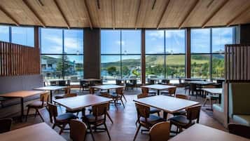 A restaurant with large windows, wooden ceiling, and multiple tables and chairs.