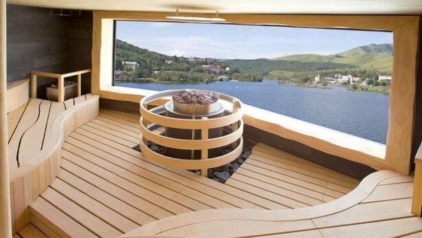 Una terraza de madera con una zona de estar circular y vistas a un lago y colinas.