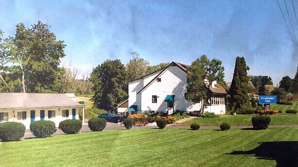 A white building with a green awning, surrounded by well-maintained lawns and trees. - Economy Inn Ithaca (Ithaca)