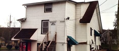 A two-story house with a front porch, a Coca-Cola vending machine, and a small staircase leading to the entrance.