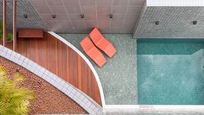 A modern pool area with a curved wooden wall, two orange lounge chairs, and a tiled floor. - Citi Hotel Residence (Caruaru)
