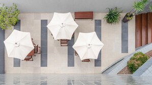 A modern outdoor seating area with white umbrellas, wooden chairs, and potted plants. - Citi Hotel Residence (Caruaru)