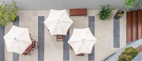 A modern outdoor seating area with white umbrellas, wooden chairs, and potted plants.