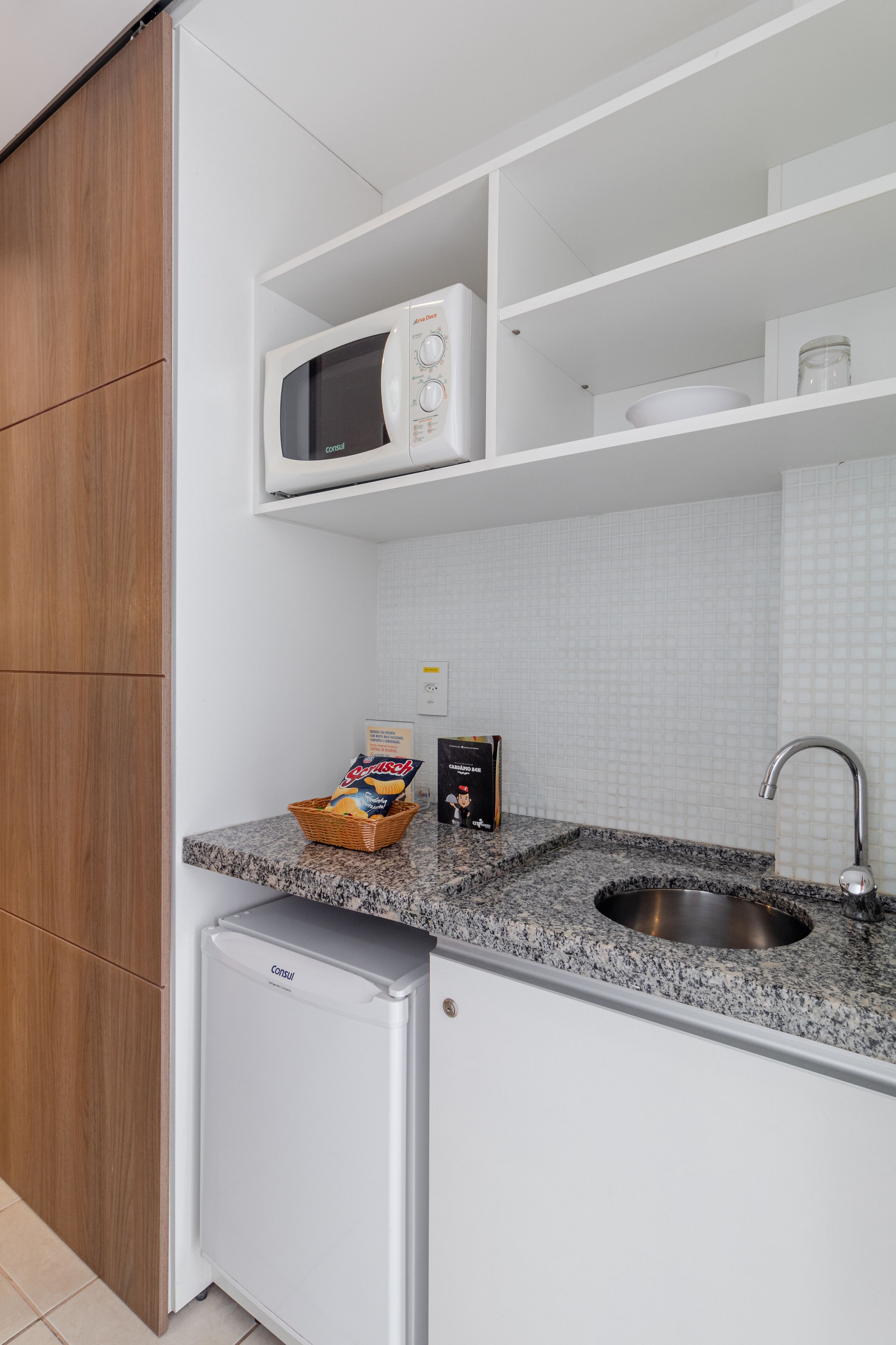 Une cuisine compacte équipée d’un four à micro-ondes, d’un petit réfrigérateur, d’un plan de travail en granit et d’un évier.