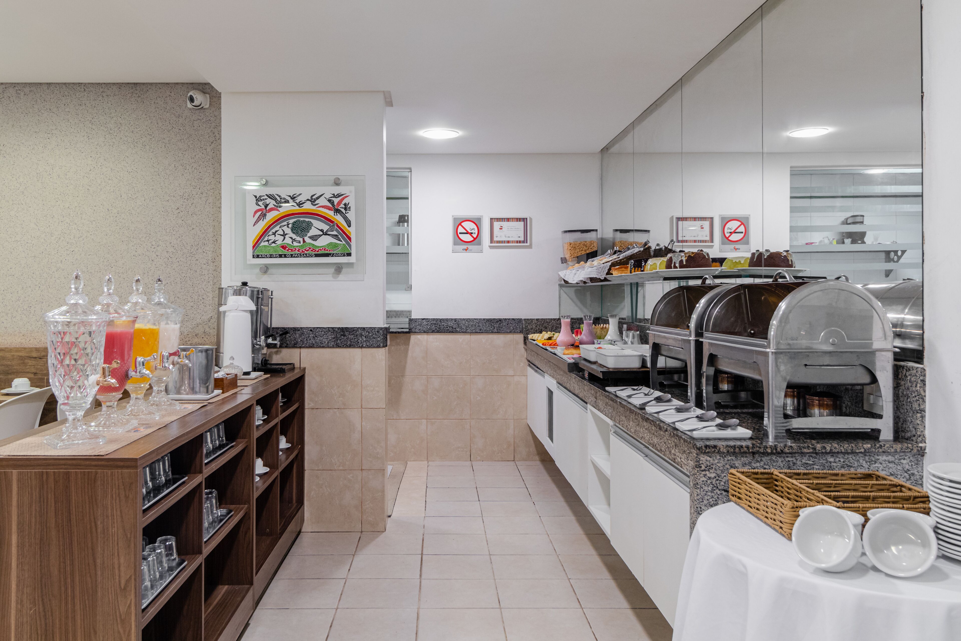 A modern breakfast area with a buffet setup, including a juice station and various food items.