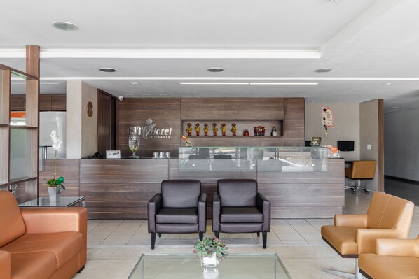 A modern hotel lobby with a reception desk, two leather armchairs, a glass coffee table, and a decorative plant. - Citi Hotel Residence (Caruaru)