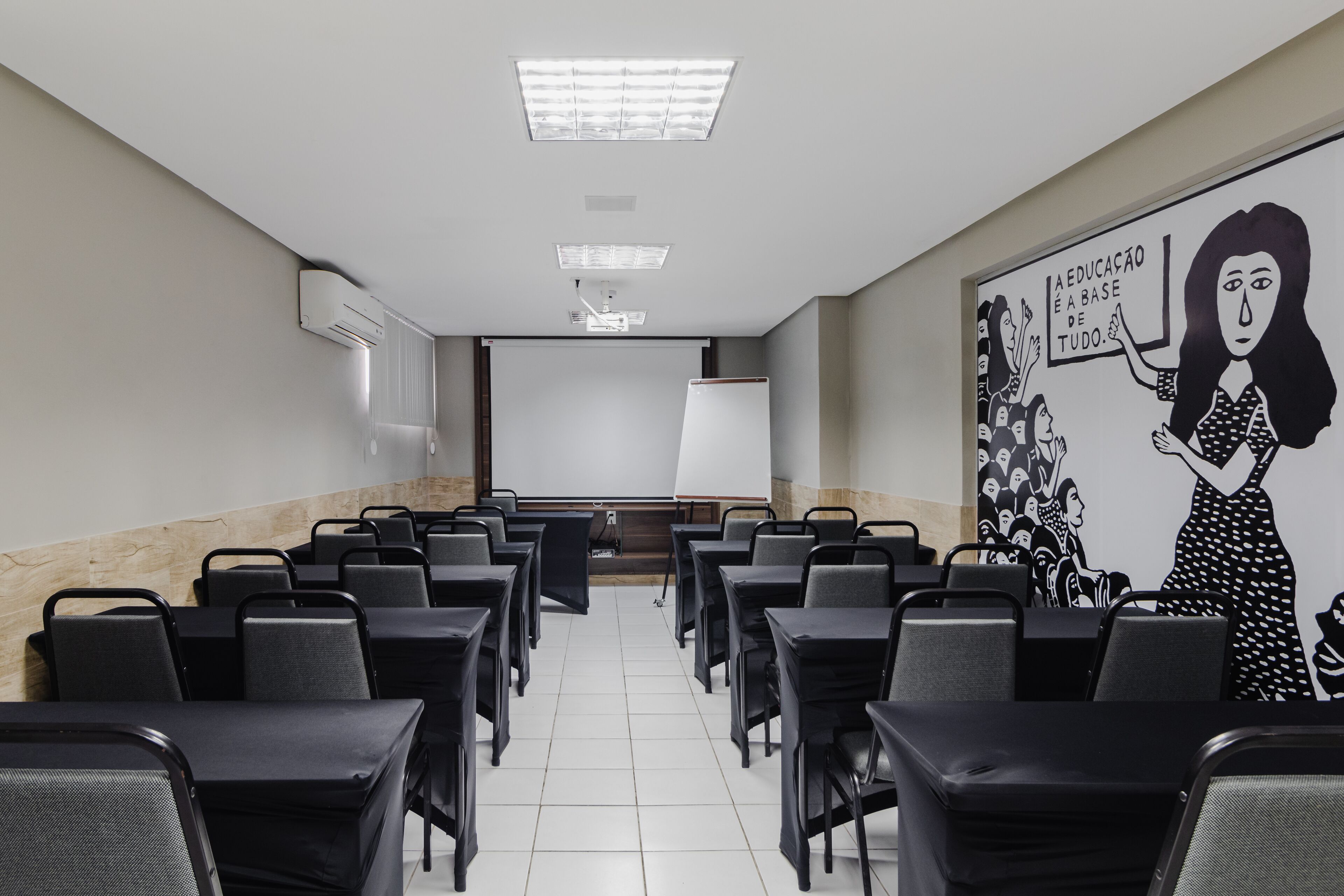Une salle de conférence avec des rangées de chaises, un écran de projection et une fresque murale.