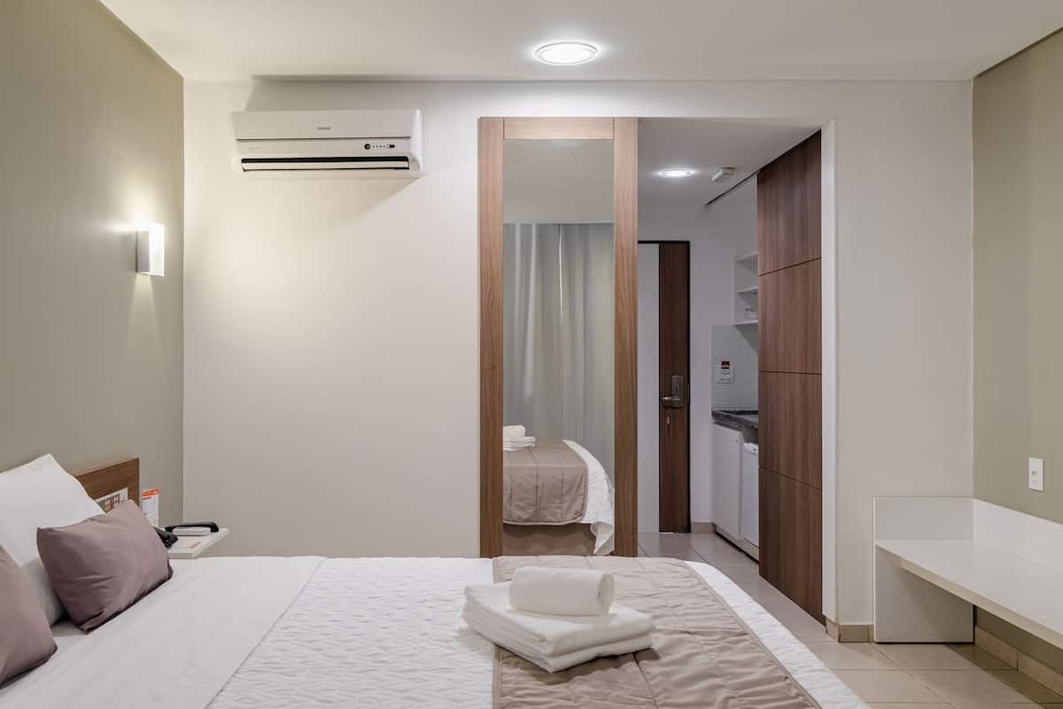 Een hotelkamer met een bed, nachtkastje, spiegel, kledingkast en een airconditioning.