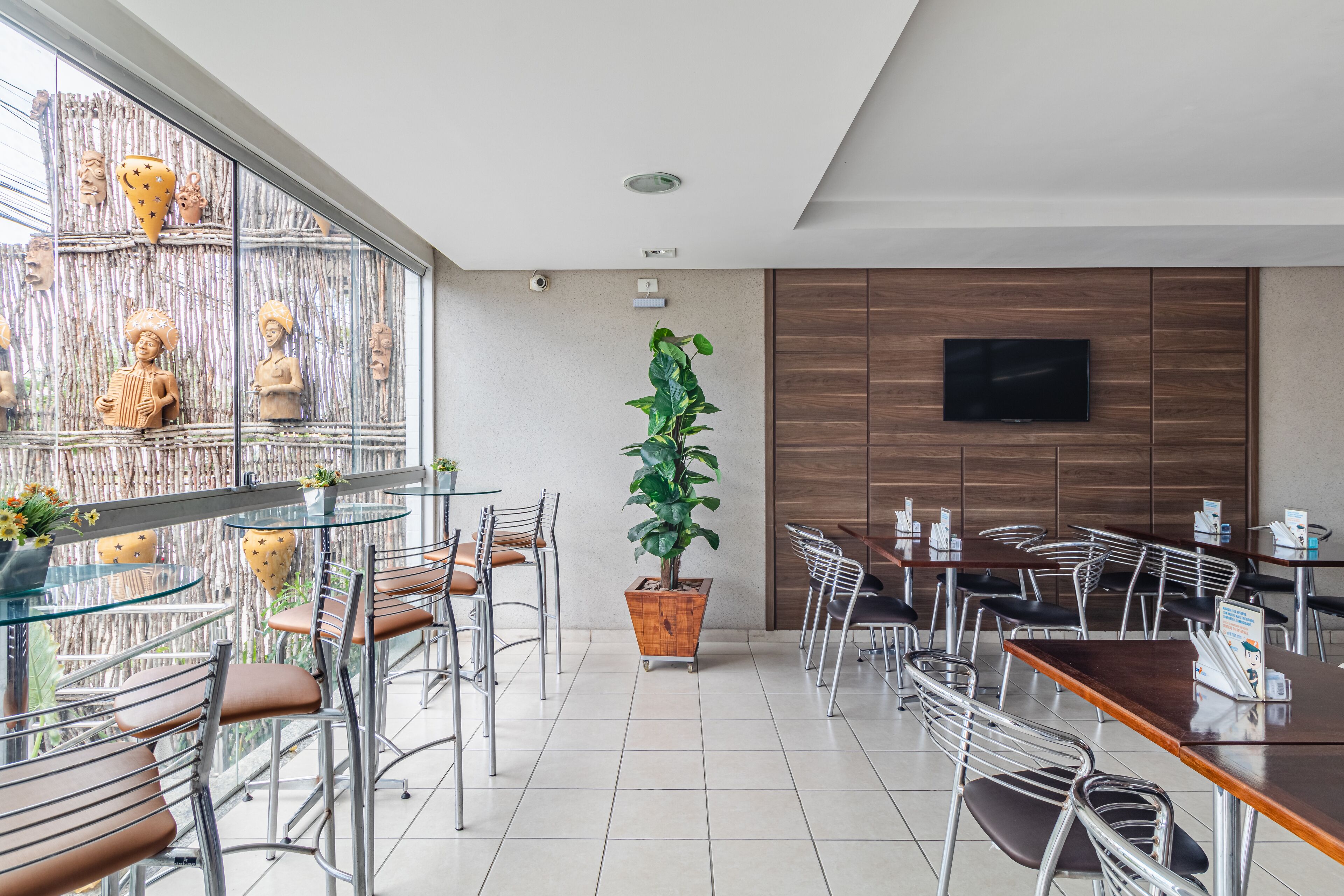 Un restaurante moderno con mesas de vidrio y sillas de metal, una planta en maceta grande y objetos decorativos en la pared.