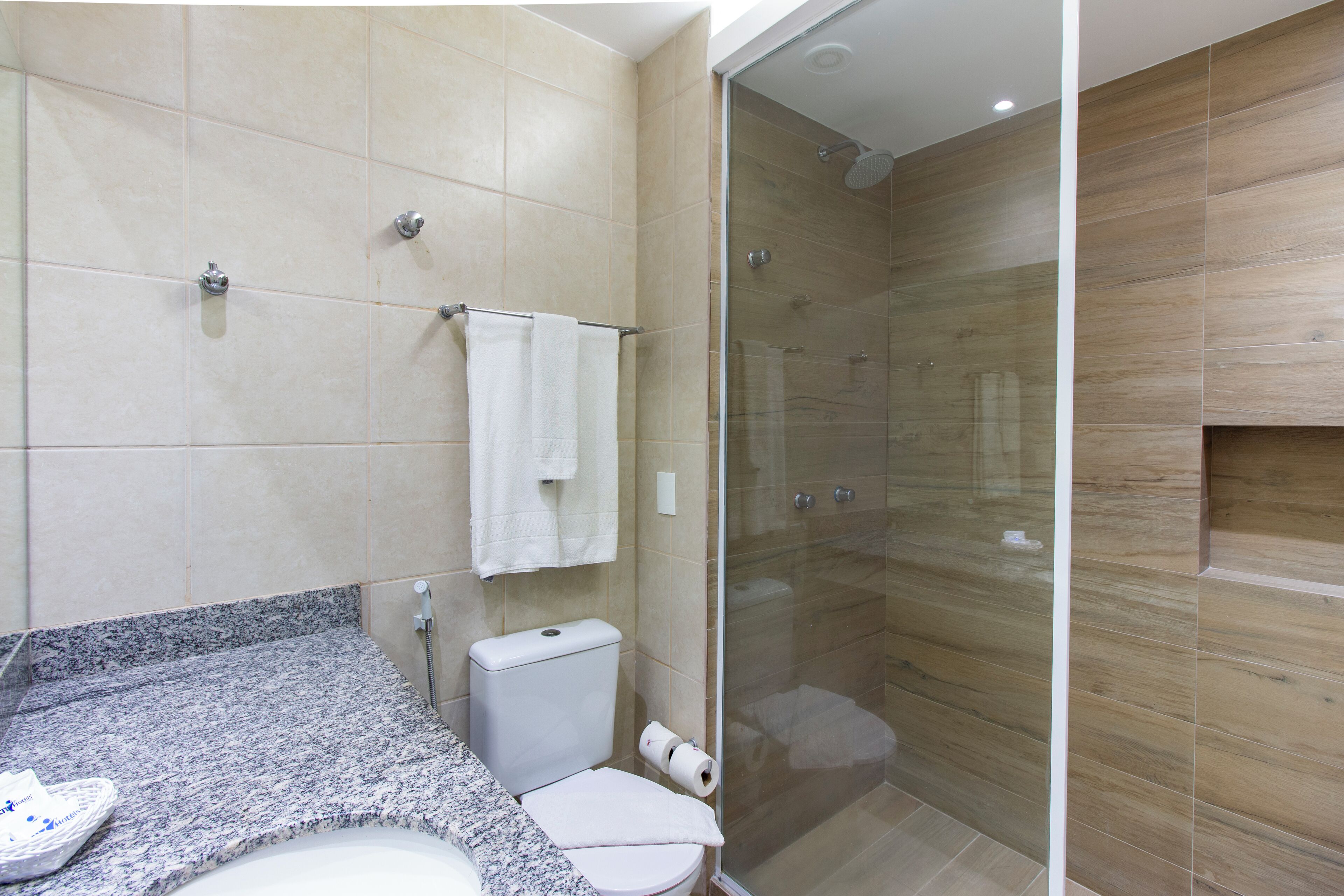 A modern bathroom with a granite countertop, a white toilet, a glass-enclosed shower, and beige tiled walls.