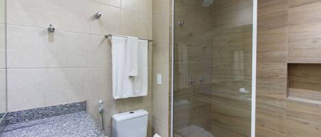 A modern bathroom with a granite countertop, a white toilet, a glass-enclosed shower, and beige tiled walls.