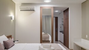 A hotel room with a bed, a bedside table, a mirror, a wardrobe, and an air conditioning unit. - Citi Hotel Residence (Caruaru)