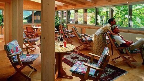 Um quarto espaçoso com vigas de madeira e janelas amplas, com várias cadeiras de madeira e uma mesa central.
