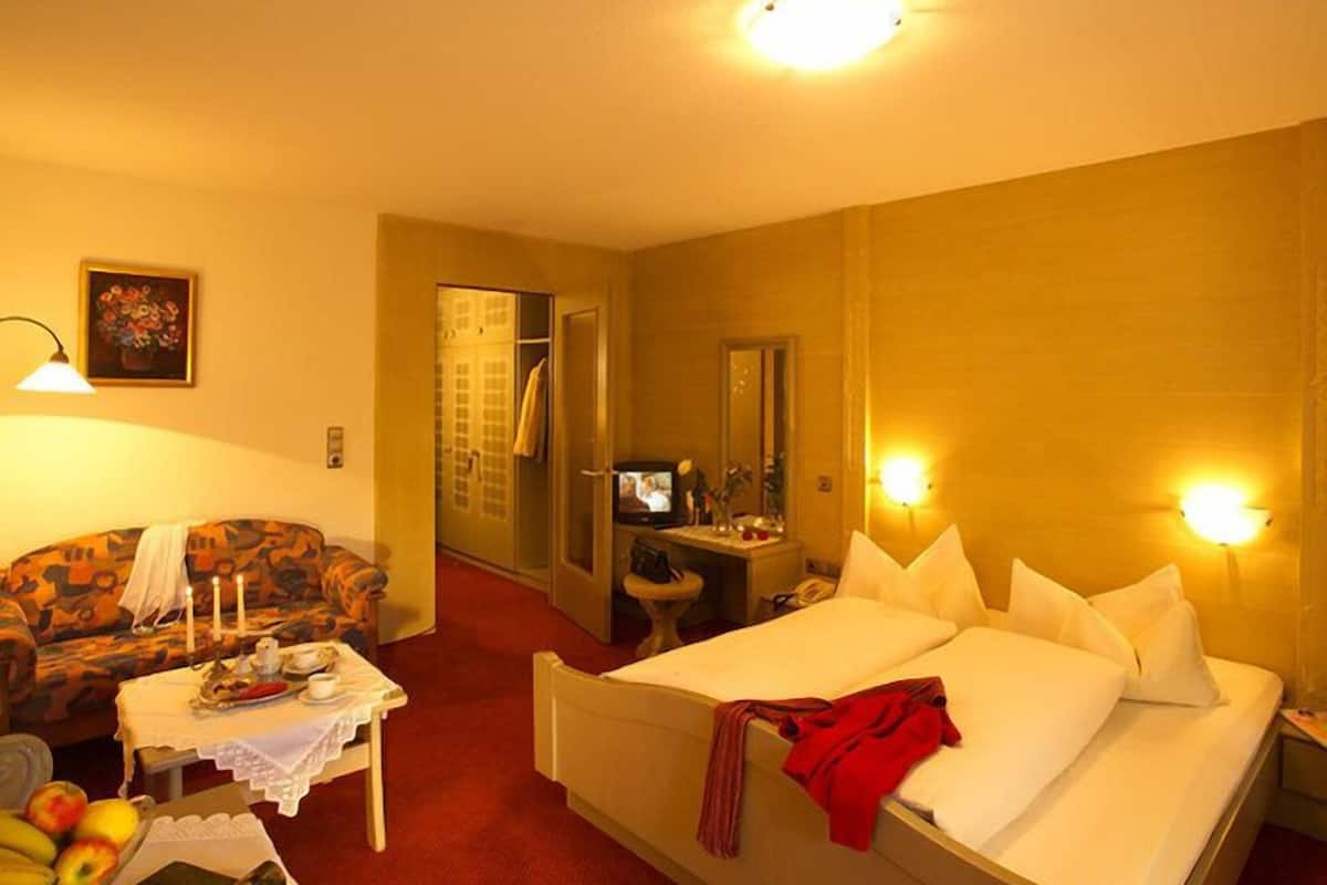 A hotel room with a bed, a sofa, a small table with apples and a candle, a television, and a mirror.