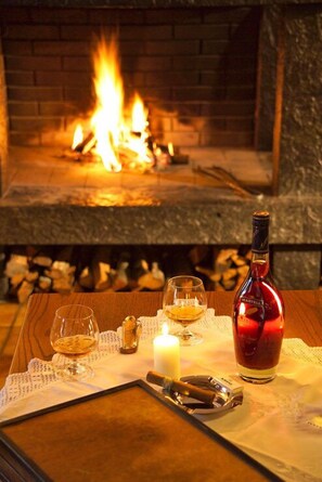 A table with glasses, a bottle, a candle, and a fireplace in the background. - Sporthotel Krone (Schoppernau)