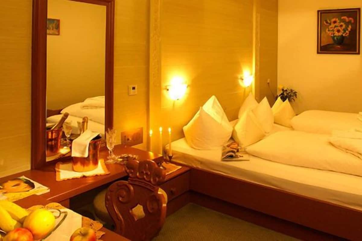 A hotel room with a large bed, a bedside table with a lamp, a mirror, and a wall-mounted light fixture.