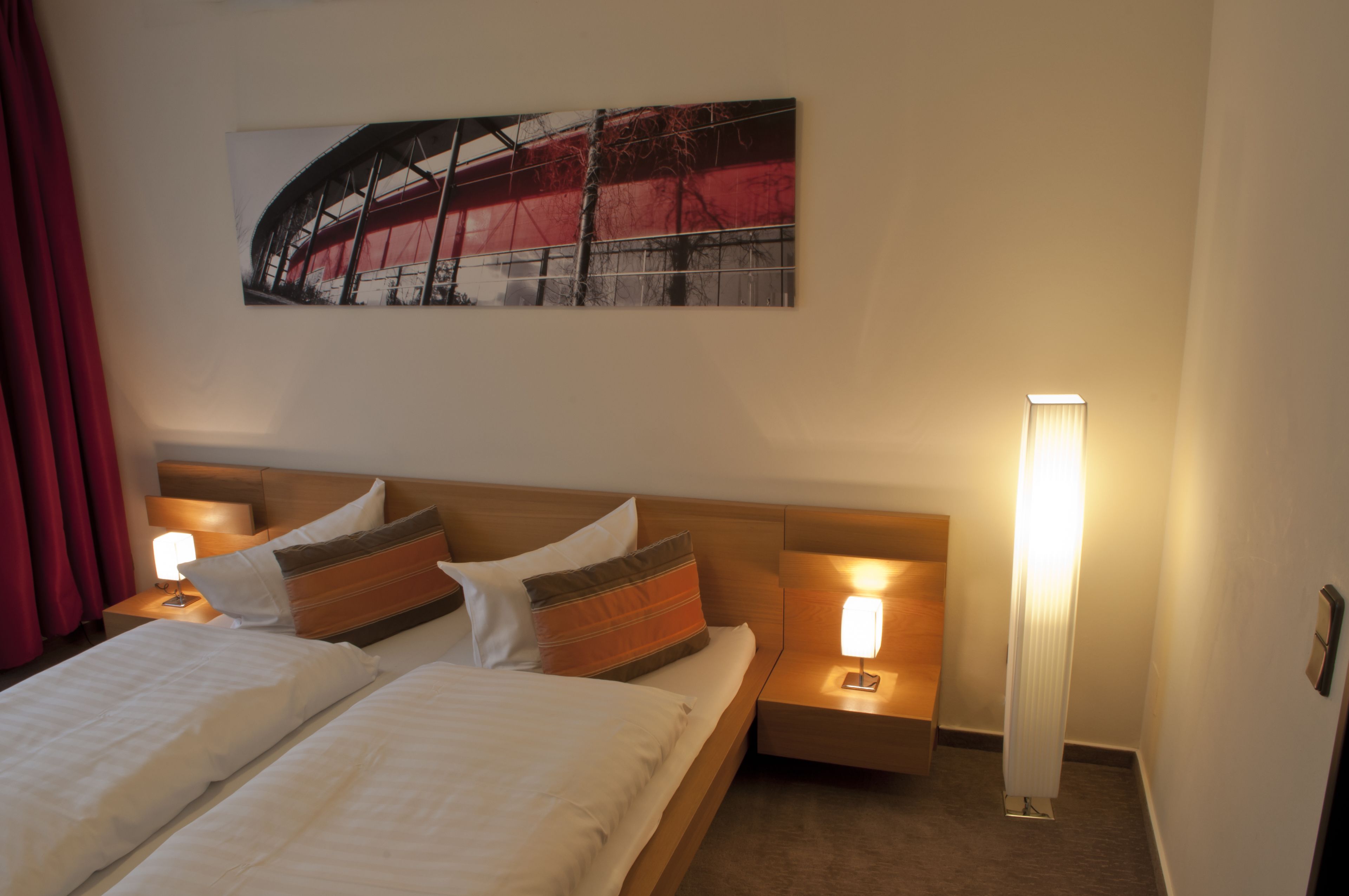 A hotel room with a bed, two bedside tables with lamps, a wall-mounted artwork, and a red curtain.