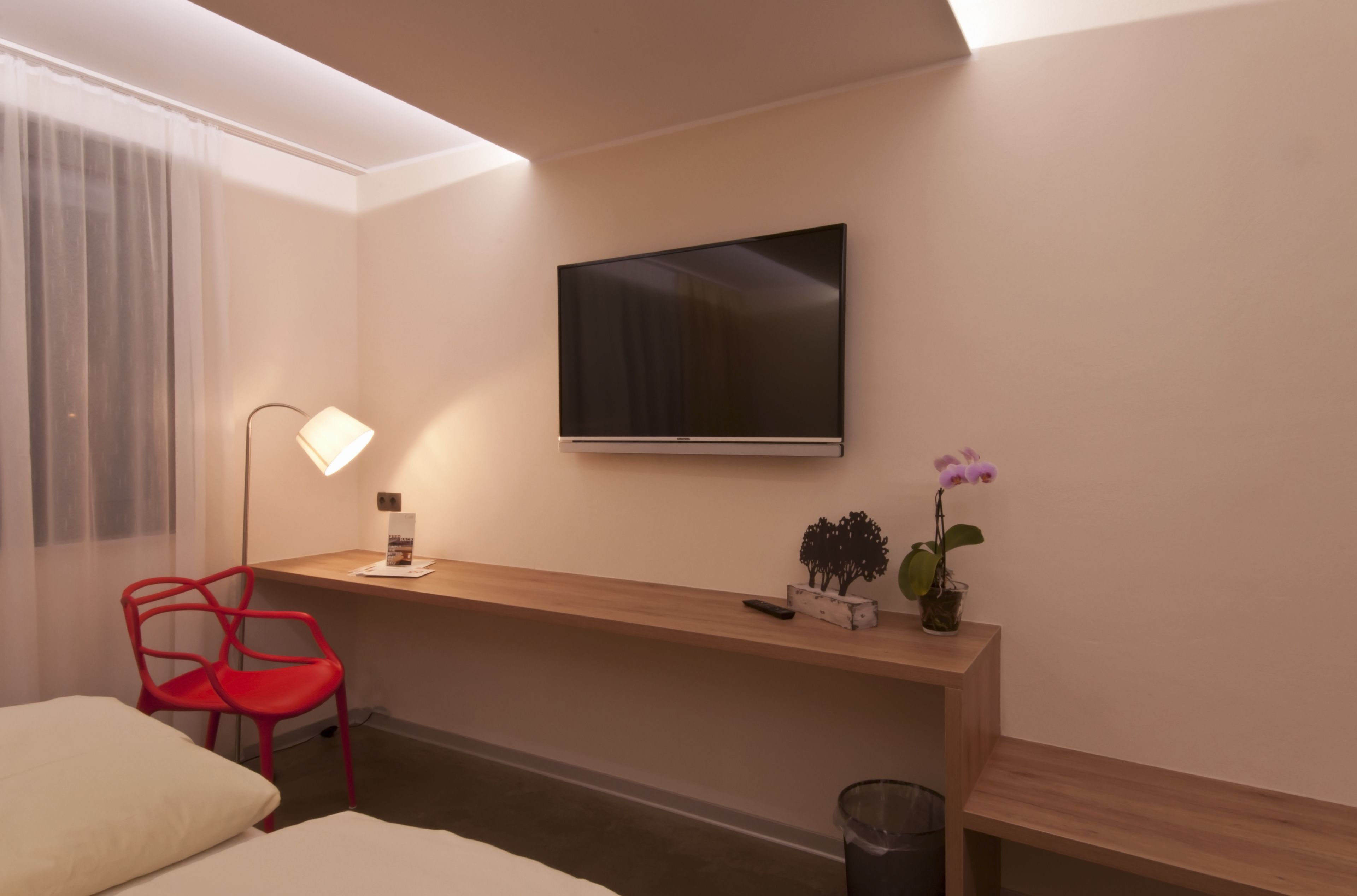 Une chambre d’hôtel avec un lit, un bureau doté d’une lampe, une télévision et une petite plante.