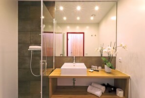 Un baño moderno con tocador de madera, un lavabo blanco, cabina de ducha de cristal y un espejo que refleja la habitación.