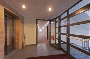 Un pasillo moderno de hotel con paneles de madera, un extintor y una puerta de vidrio que da a un espacio exterior.