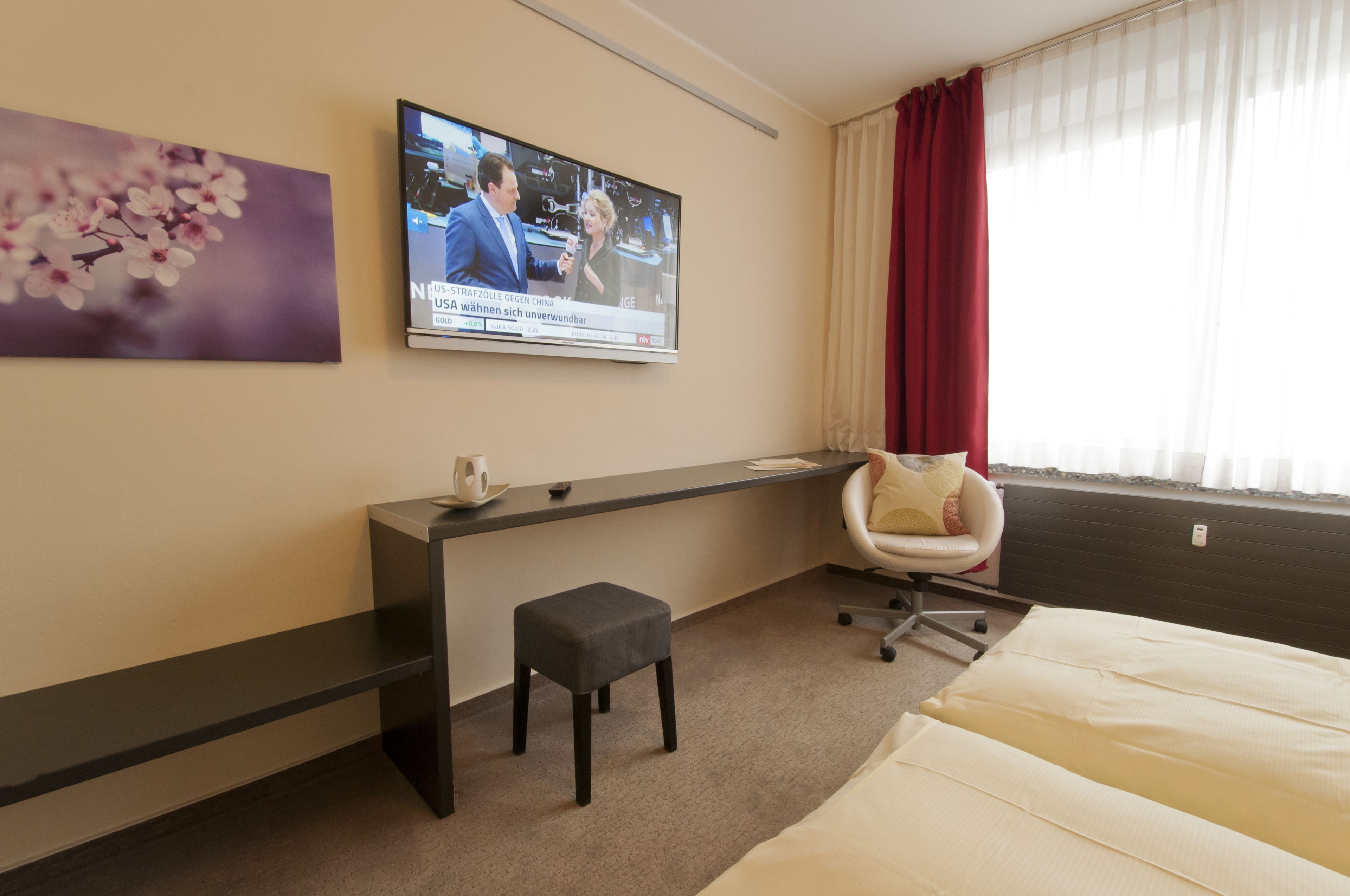 Habitación de hotel con cama, escritorio, silla, televisor en la pared y ventana con cortinas.