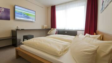 Ein modernes Hotelzimmer mit einem Bett, einem Wandfernseher, einem Schreibtisch und einem Fenster mit Vorhängen.